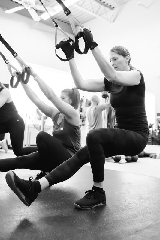 UPLIFT Women in class performing a TRX pistol squat in Black and White