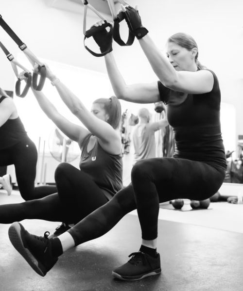 UPLIFT Women in class performing a TRX pistol squat in Black and White